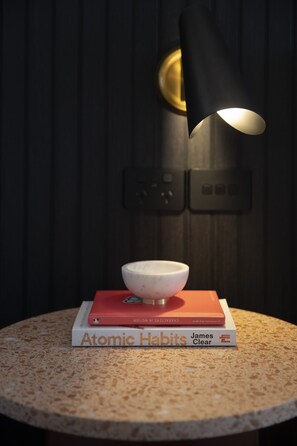 A round table with a bowl and two books, a black lamp, and a wall-mounted switch. - The Sebel Sydney Martin Place (Sydney)