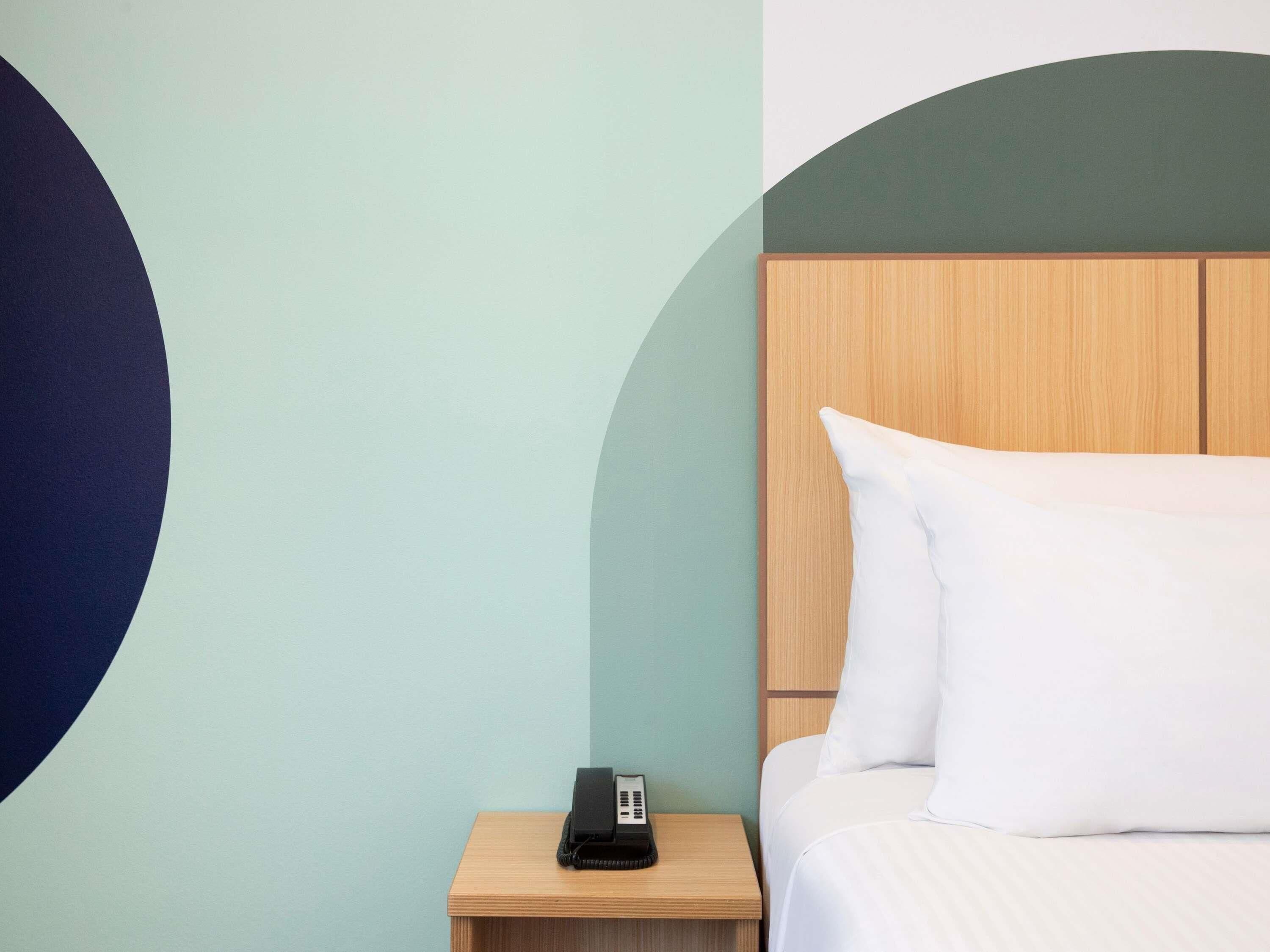 A hotel room with a bed, a nightstand with a telephone, and a wall with a geometric design.