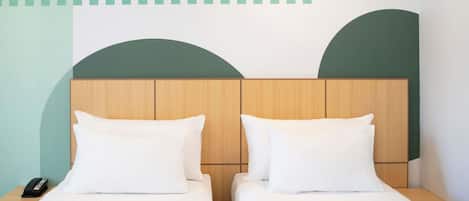 Habitación de hotel con dos camas individuales, cabeceros de madera, ropa de cama blanca, un teléfono en la mesita de noche y una pared con motivos geométricos.