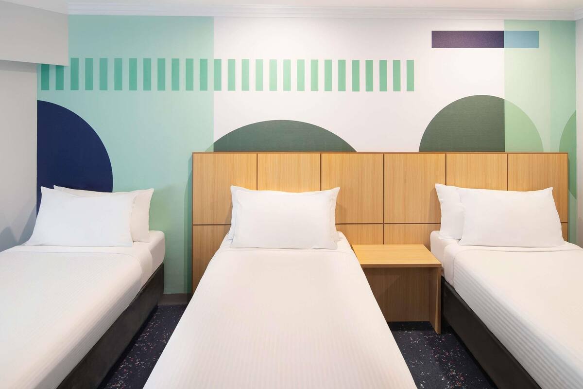A hotel room with two single beds, a wooden headboard, and a wall with geometric patterns.