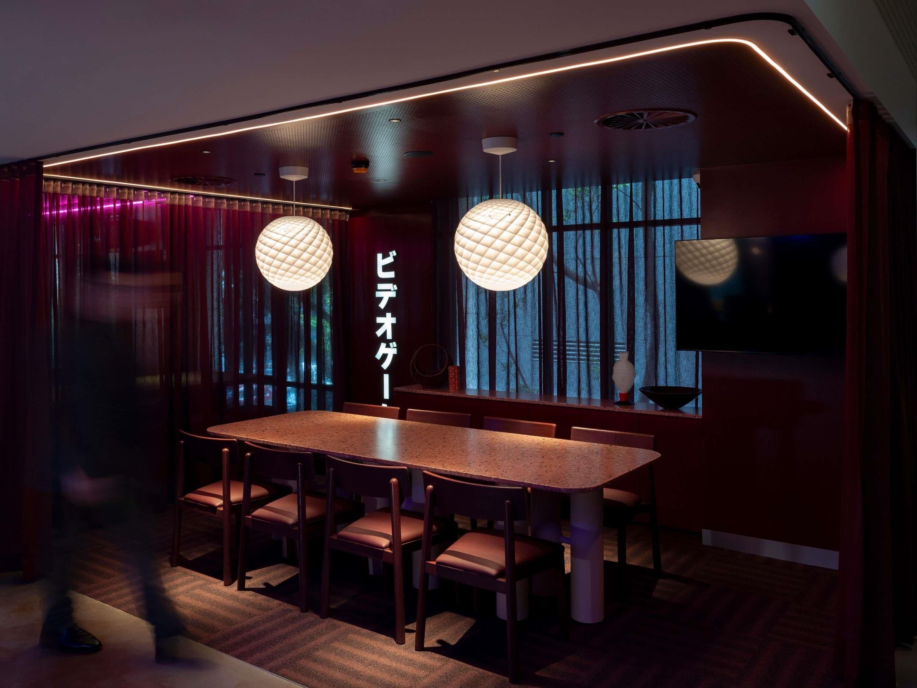 A modern dining area with a round table, chairs, pendant lights, and a large window with curtains.