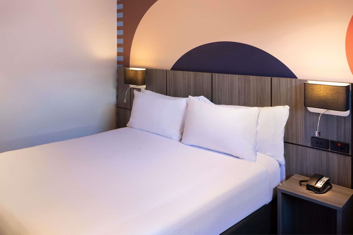 A hotel room with a large bed, two bedside lamps, a nightstand with a telephone, and a wall-mounted light.