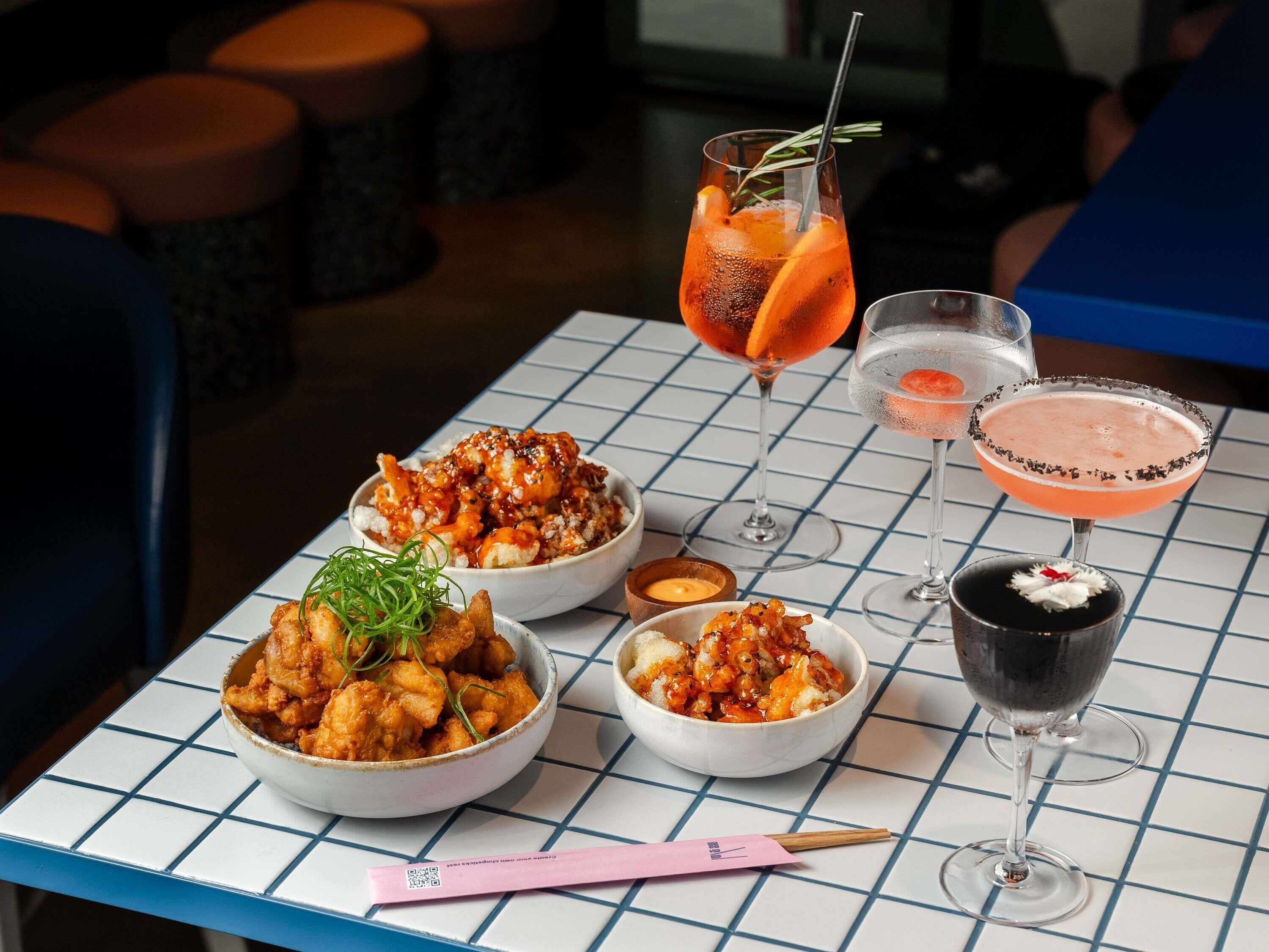 A table with three bowls of fried chicken, two cocktails, and a dessert.