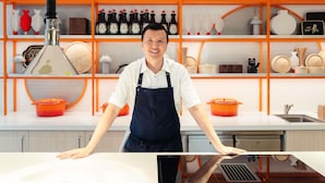 A kitchen with modern appliances, a person standing behind a counter, and shelves with kitchenware and bottles. - ibis Styles Sydney Central (Sydney)