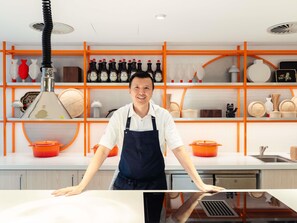 A kitchen with modern appliances, a person standing behind a counter, and shelves with kitchenware and bottles. - ibis Styles Sydney Central (Sydney)
