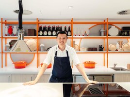 Cozinha com eletrodomésticos modernos, uma pessoa em frente a um balcão e prateleiras com utensílios de cozinha e garrafas.