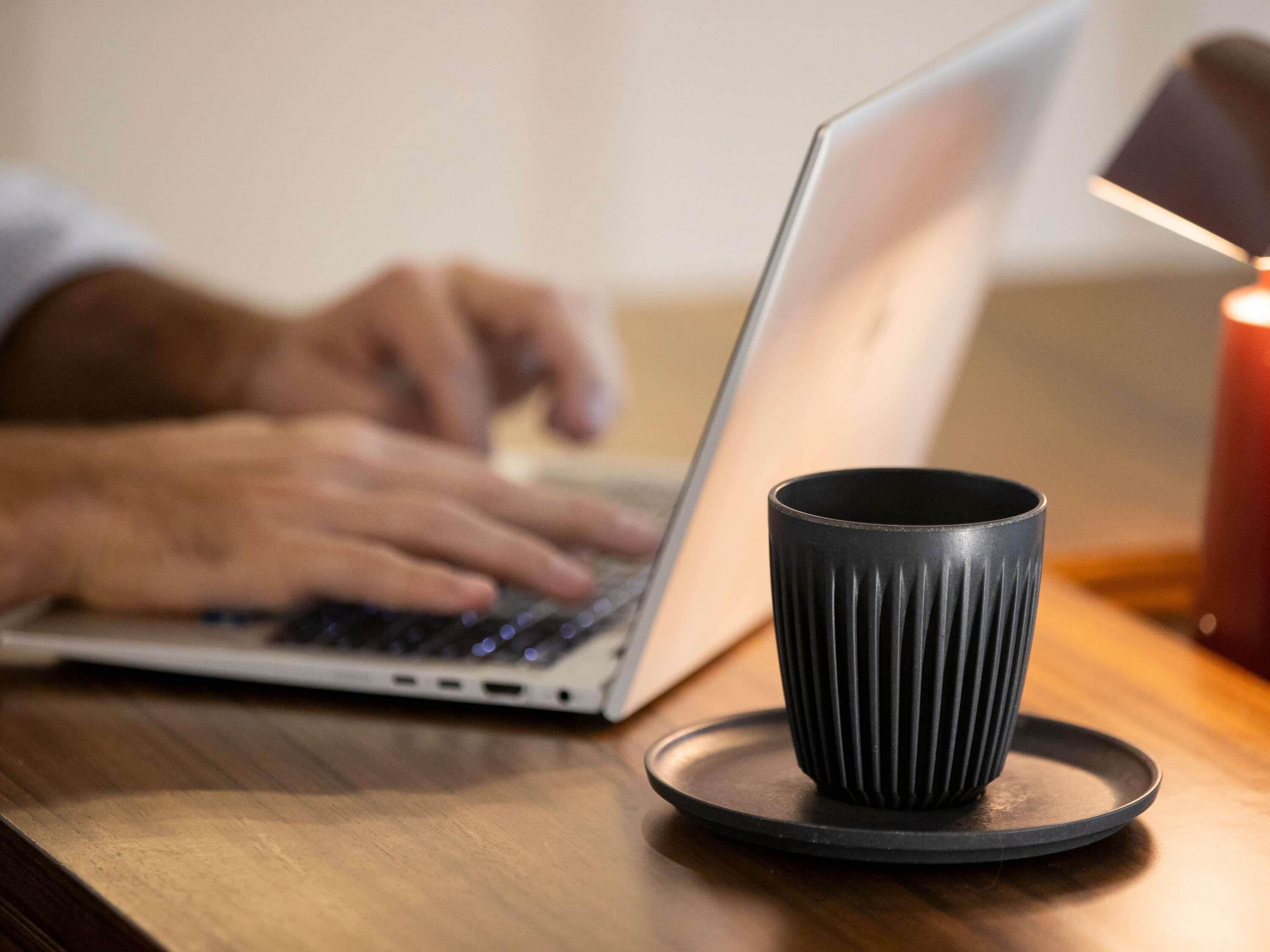 A laptop on a wooden table with a black mug on a coaster.