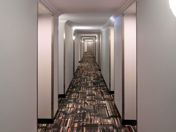 A long, narrow hotel hallway with a patterned carpet and white walls.