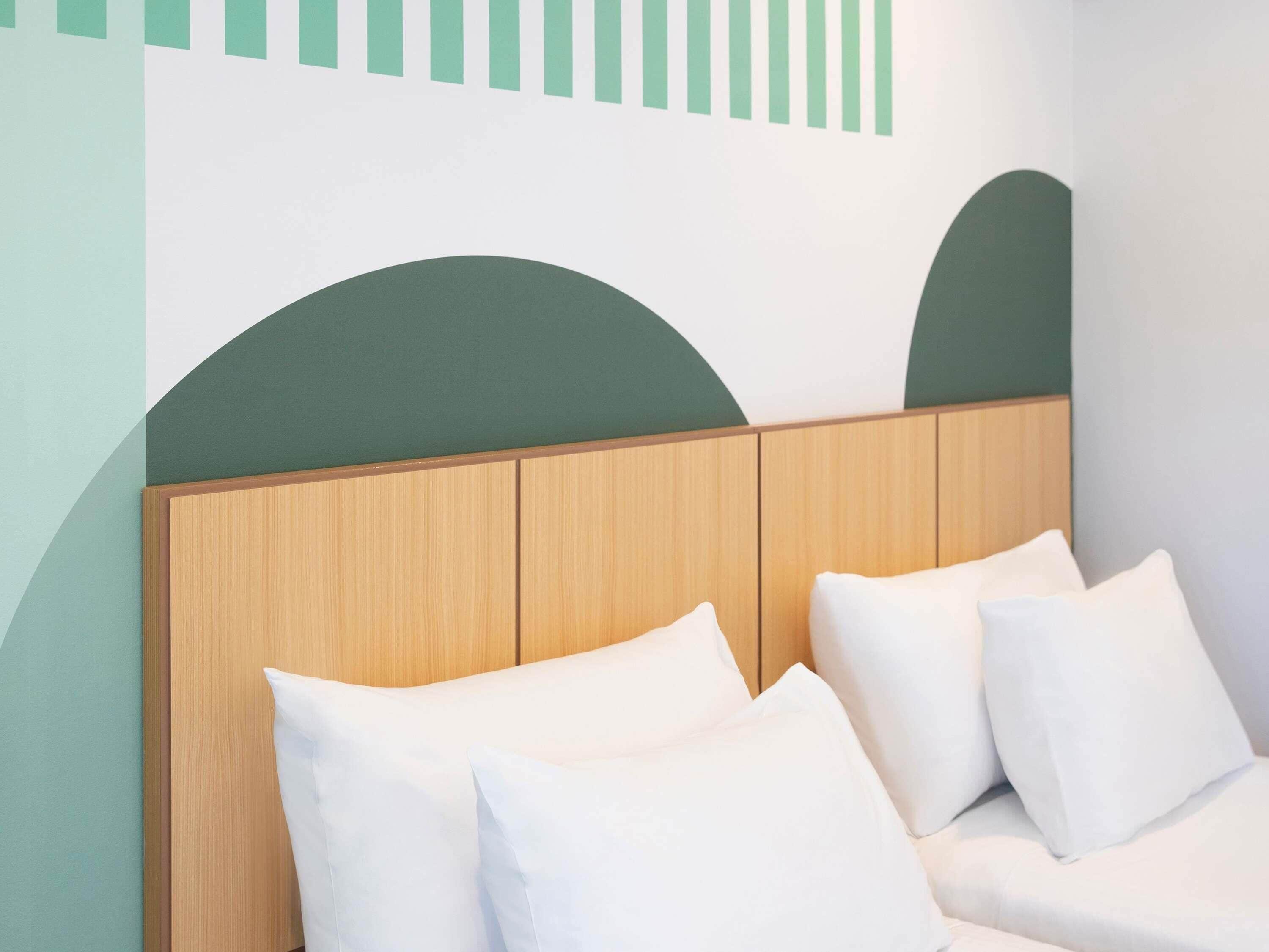 Cama com cabeceira de madeira e almofadas brancas em quarto com design geométrico na parede.