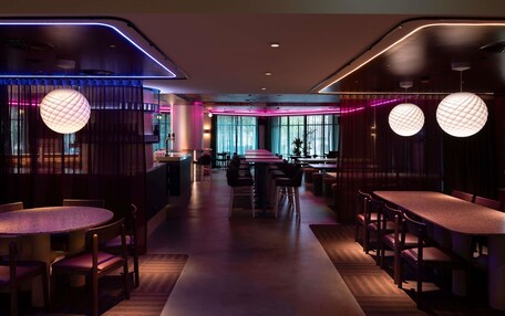 A modern restaurant with round tables, ambient lighting, and a central walkway.