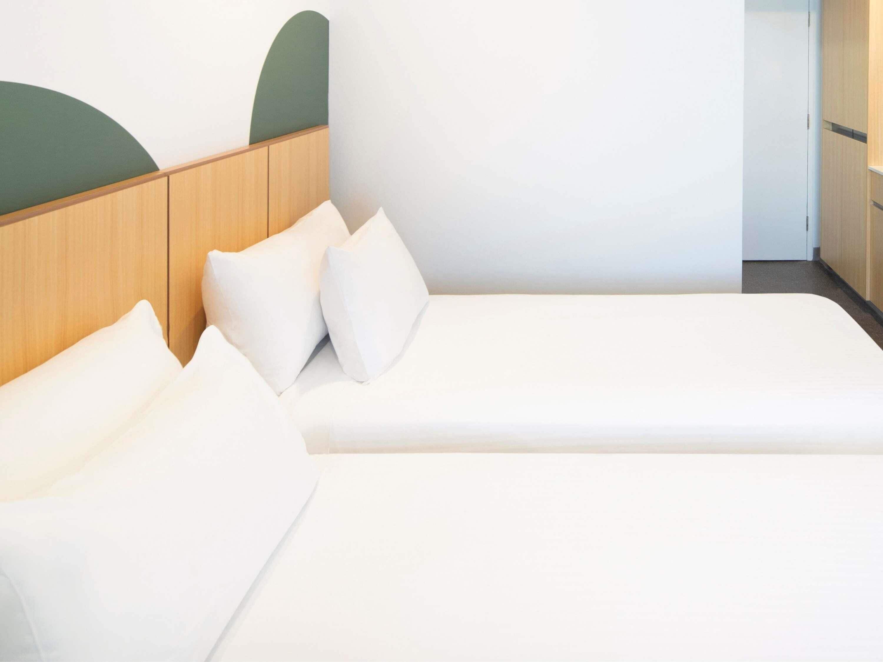 A modern hotel room with a wooden headboard, a single bed with white bedding, and a minimalist design.