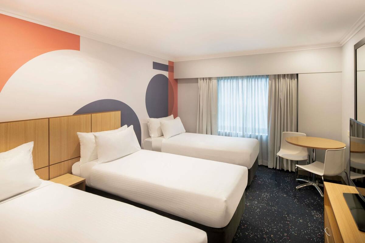 A hotel room with three beds, a desk, a chair, and a small table.