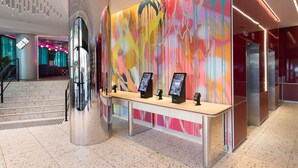 A modern lobby with a reception desk, digital information kiosks, and a vibrant abstract mural. - ibis Styles Sydney Central (Sydney)