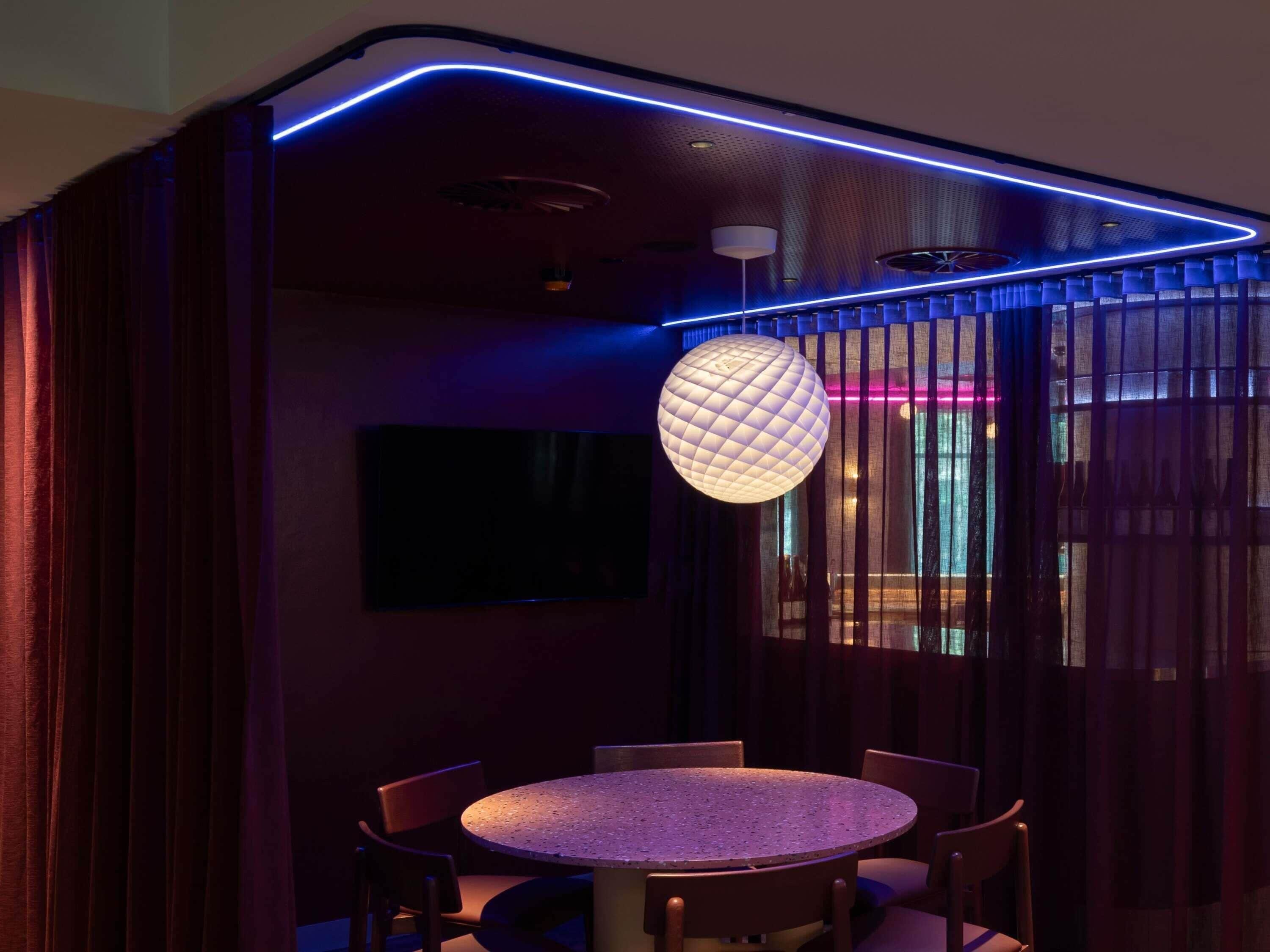 Un espace repas moderne avec une table ronde, des chaises, un luminaire suspendu de forme sphérique et un téléviseur fixé au mur.