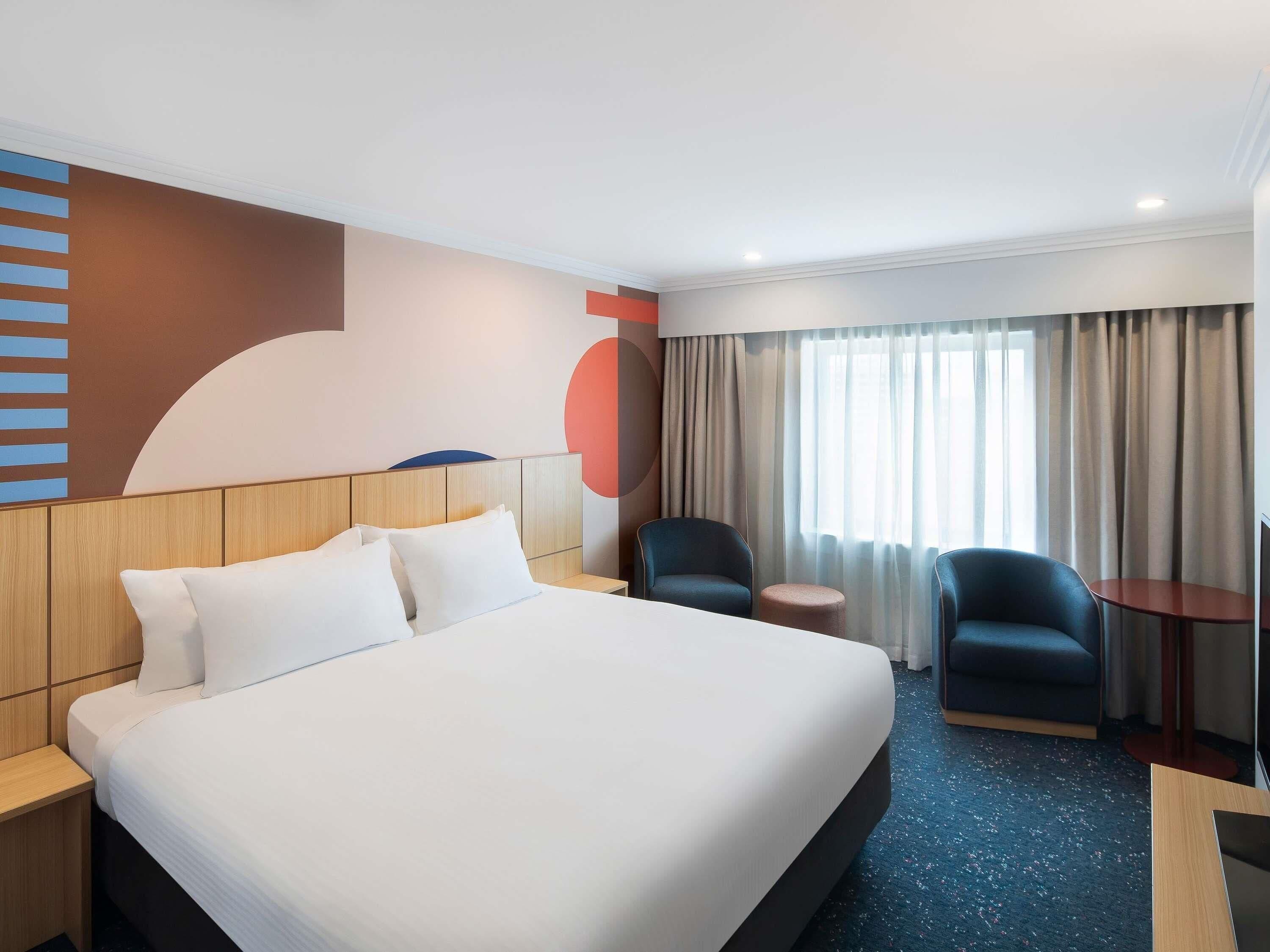 A hotel room with a large bed, two chairs, a small table, and a TV.