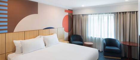 Hotellihuone, jossa on suuri sänky, kaksi tuolia, pieni pöytä ja televisio.