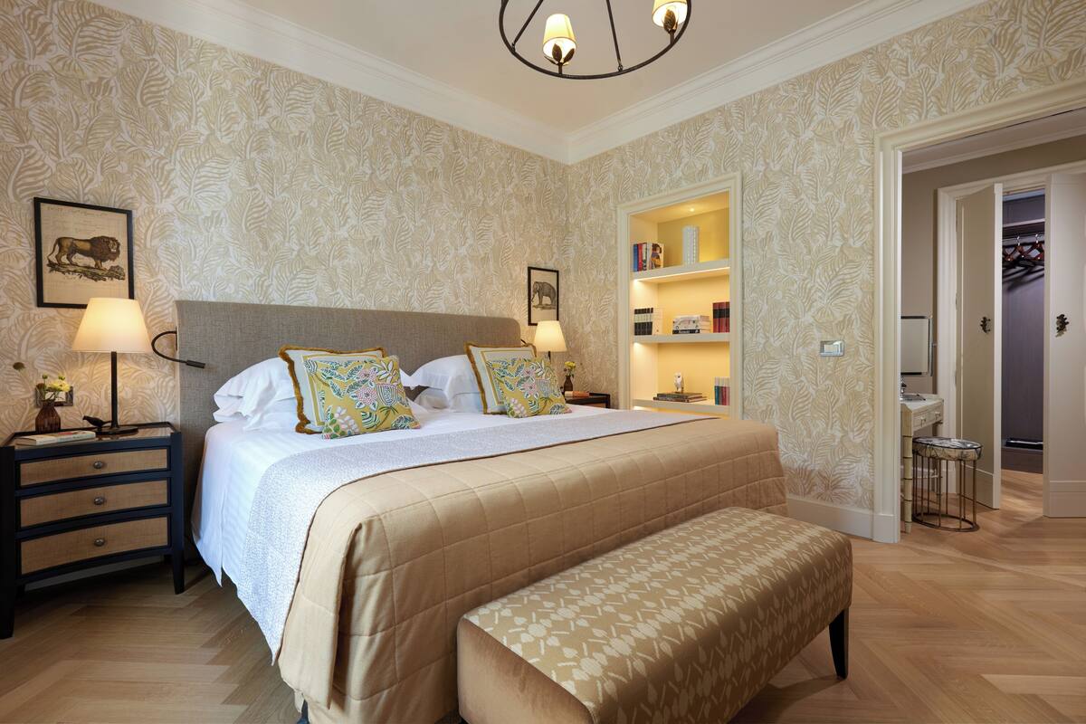 A bedroom with a large bed, bedside tables, a bench, a wardrobe, and a small stool.