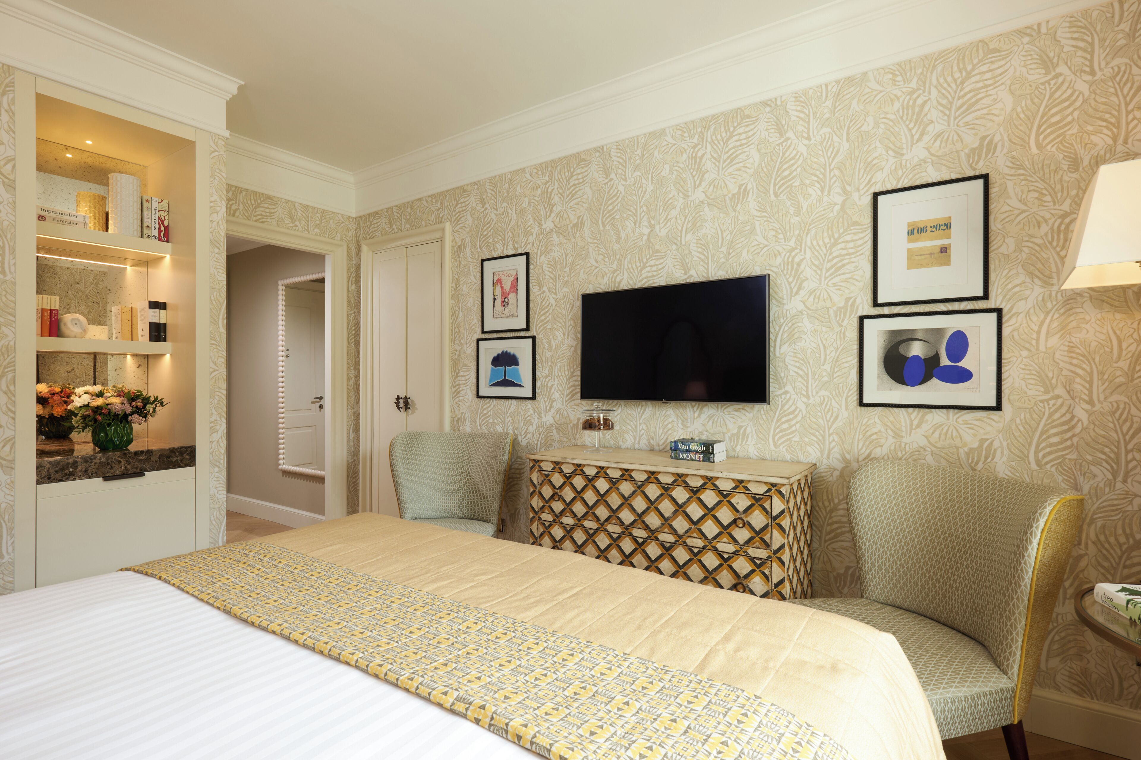 A hotel room with a bed, a TV, a vanity with a mirror, and a wall with framed pictures.