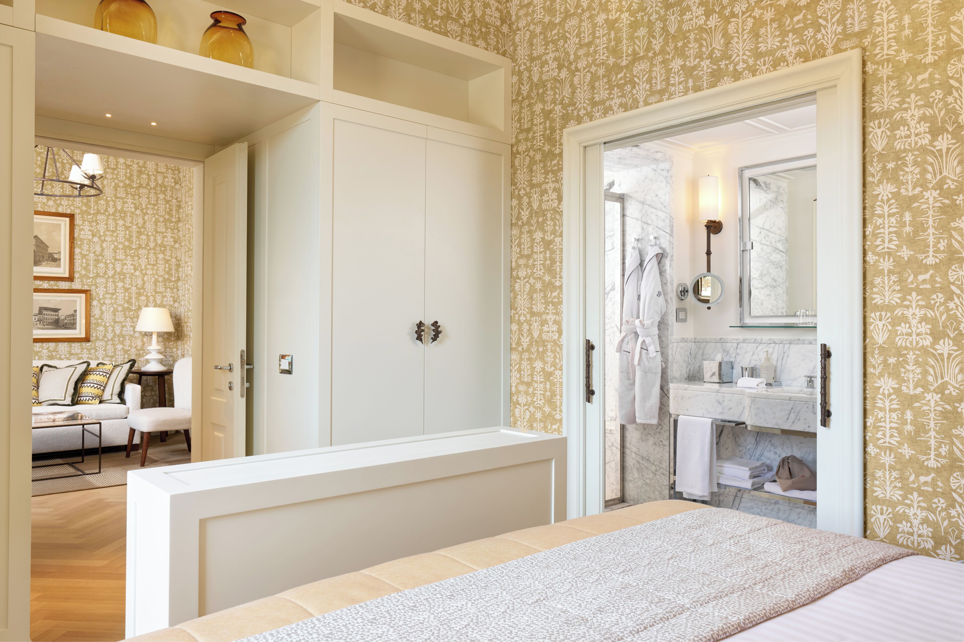 Ein Schlafzimmer mit Bett, Kleiderschrank, Badezimmer mit Spiegel und Waschbecken sowie einem Wohnbereich mit Sofa und Lampe.