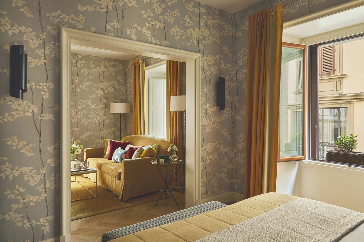 A hotel room with a sofa, a side table, a mirror, and a window with curtains.