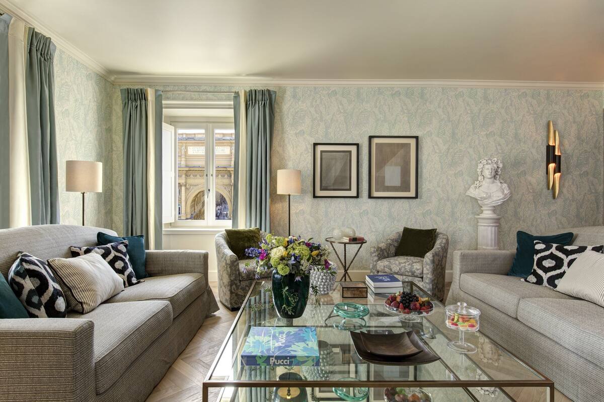 A living room with two sofas, a glass coffee table, a vase with flowers, framed pictures, and a bust sculpture.