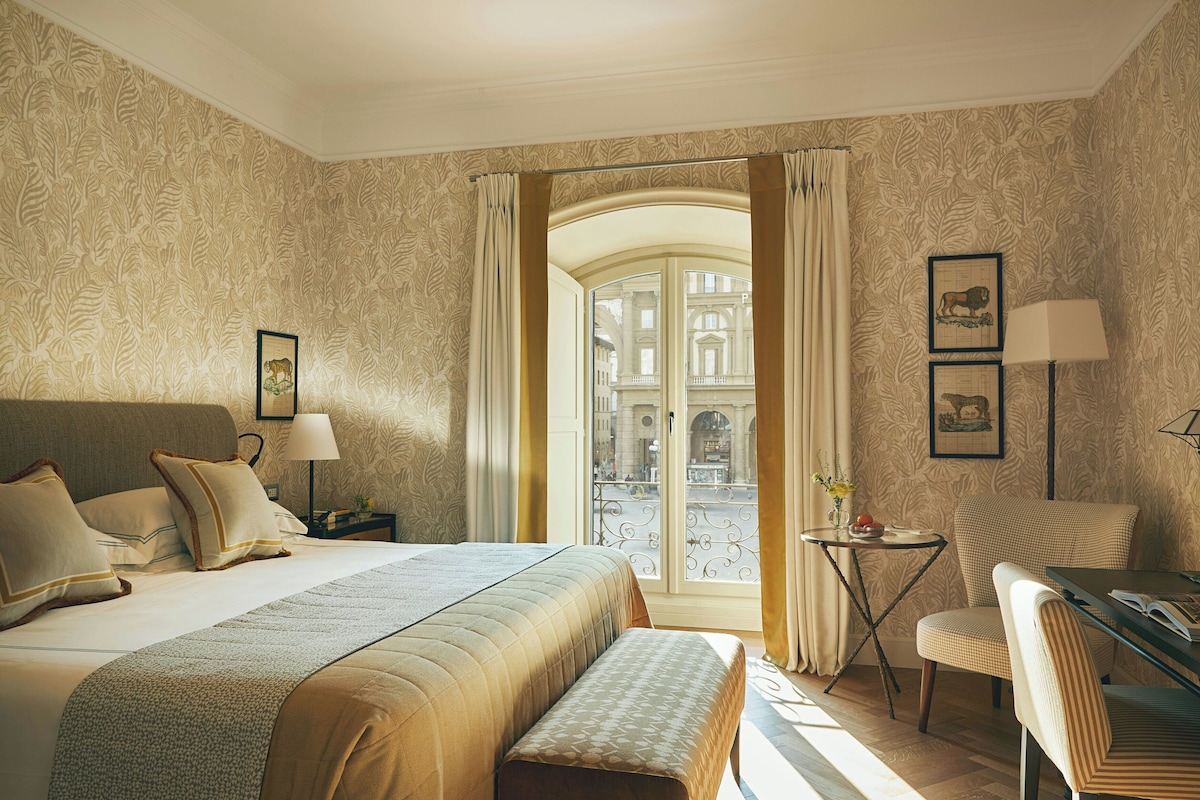 Een hotelkamer met een bed, een bureau, een stoel en uitzicht op de straat door een glazen deur.