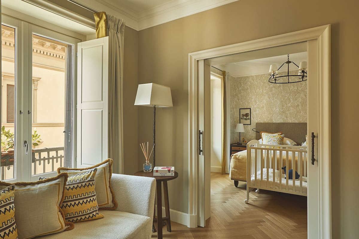 Une pièce avec un berceau blanc, une petite table avec une lampe et un canapé agrémenté de coussins à motifs.