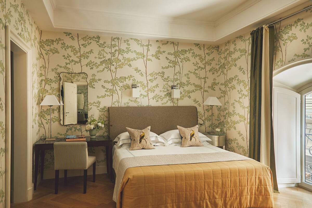 A hotel room with a bed, desk, chair, and a view of the outside.