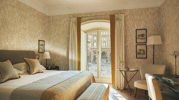 A hotel room with a bed, a desk, a chair, a small table, and a view of the street through a glass door.
