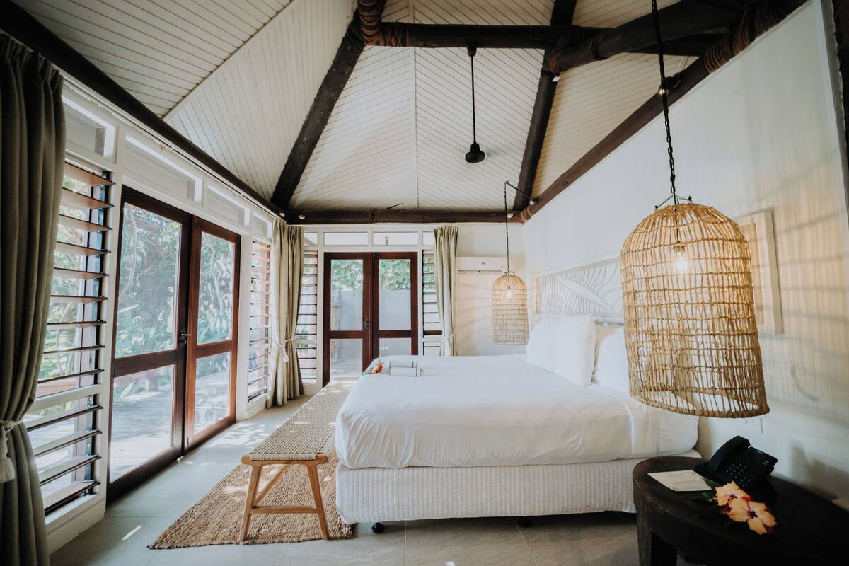A bedroom with a large bed, a hanging light fixture, and a view of the outdoors through a sliding door.