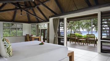 A bedroom with a large bed, a wooden ceiling, and a view of the ocean through open doors.