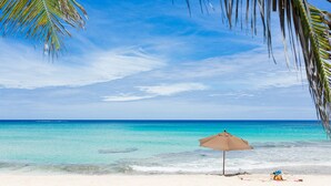 Una playa con agua turquesa cristalina, orilla de arena y una sombrilla.