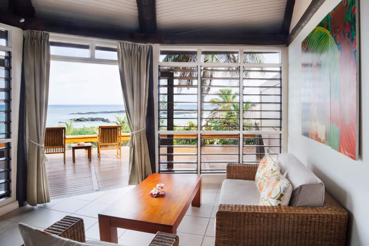 A room with a wooden table, wicker sofa, and a view of the ocean through large windows.
