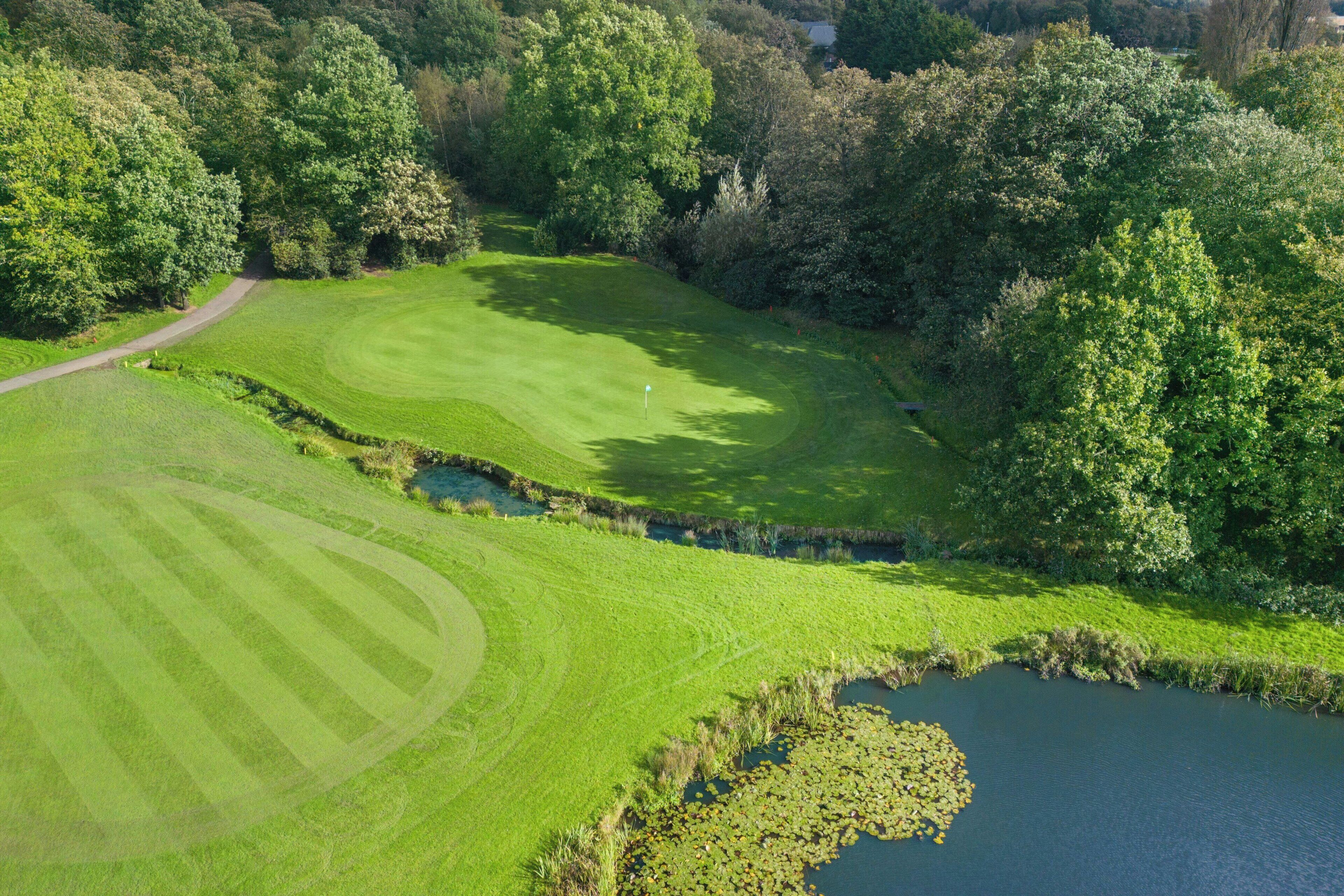 An aerial view of a golf course with a pond and dense trees.