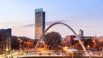 Un puente moderno con una amplia estructura en arco, rodeado de edificios urbanos y farolas.