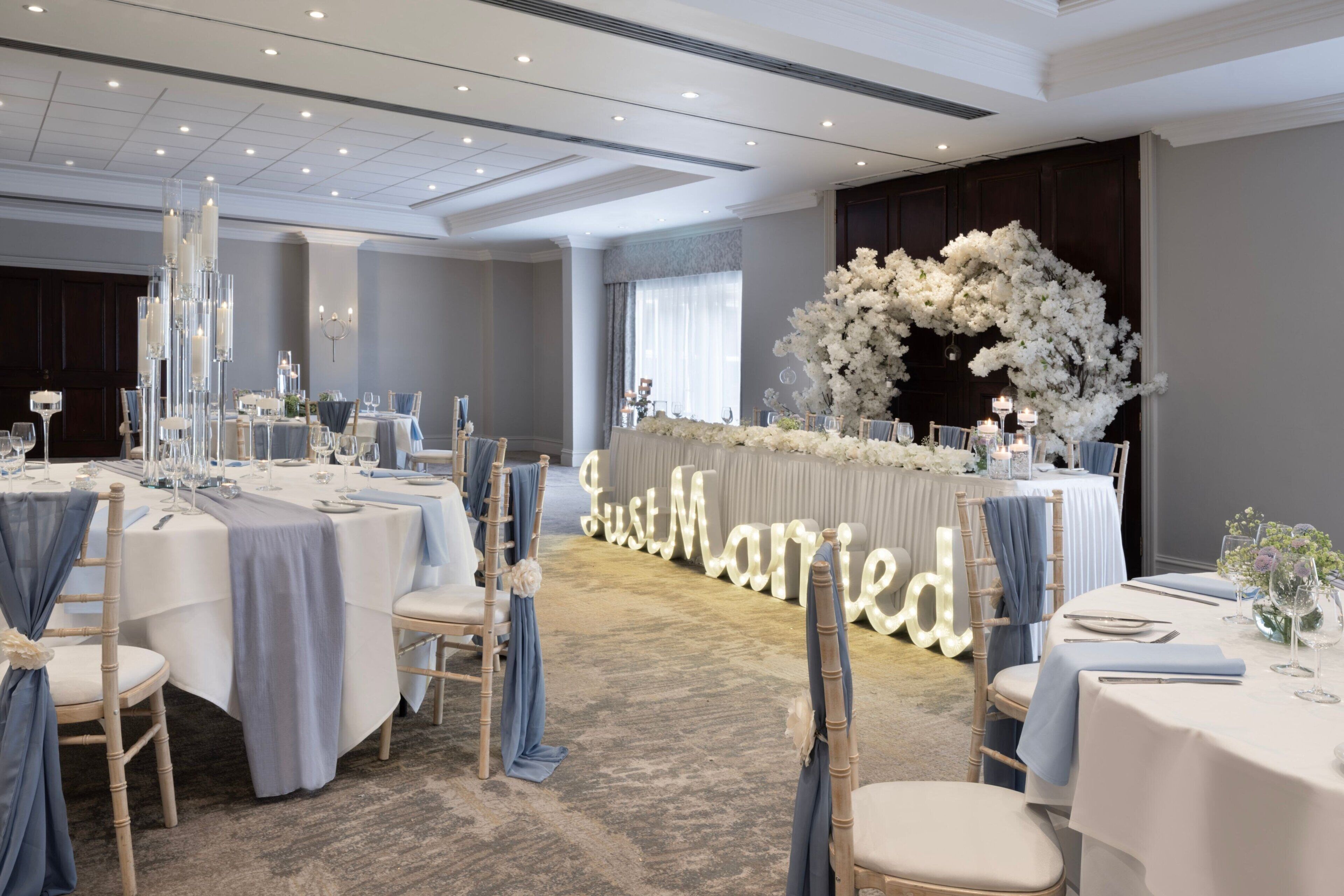 Decoración para una recepción de boda con mesas redondas, sillas y un arco floral.