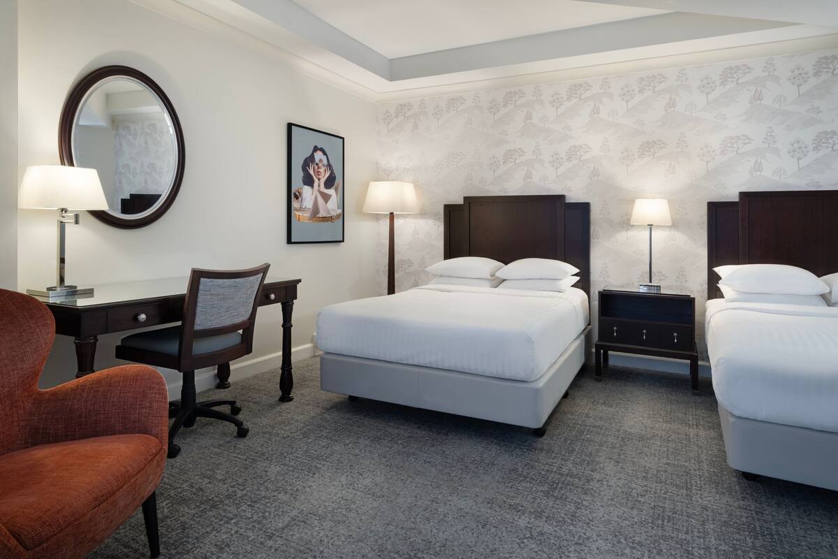 Una habitación de hotel con cama, dos mesitas de noche, un escritorio con silla y un espejo grande.
