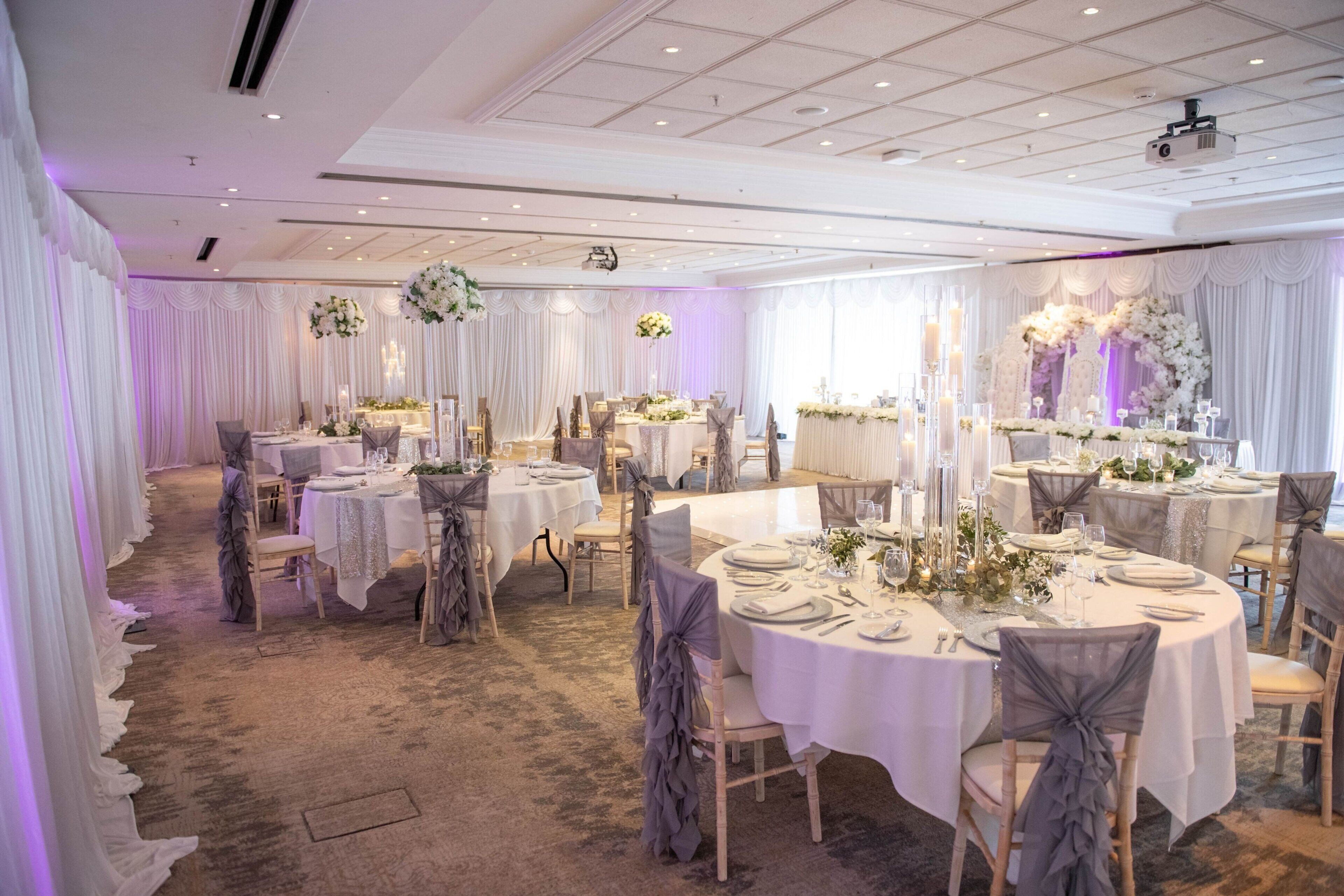 A banquet hall with round tables, white drapes, and floral centerpieces.