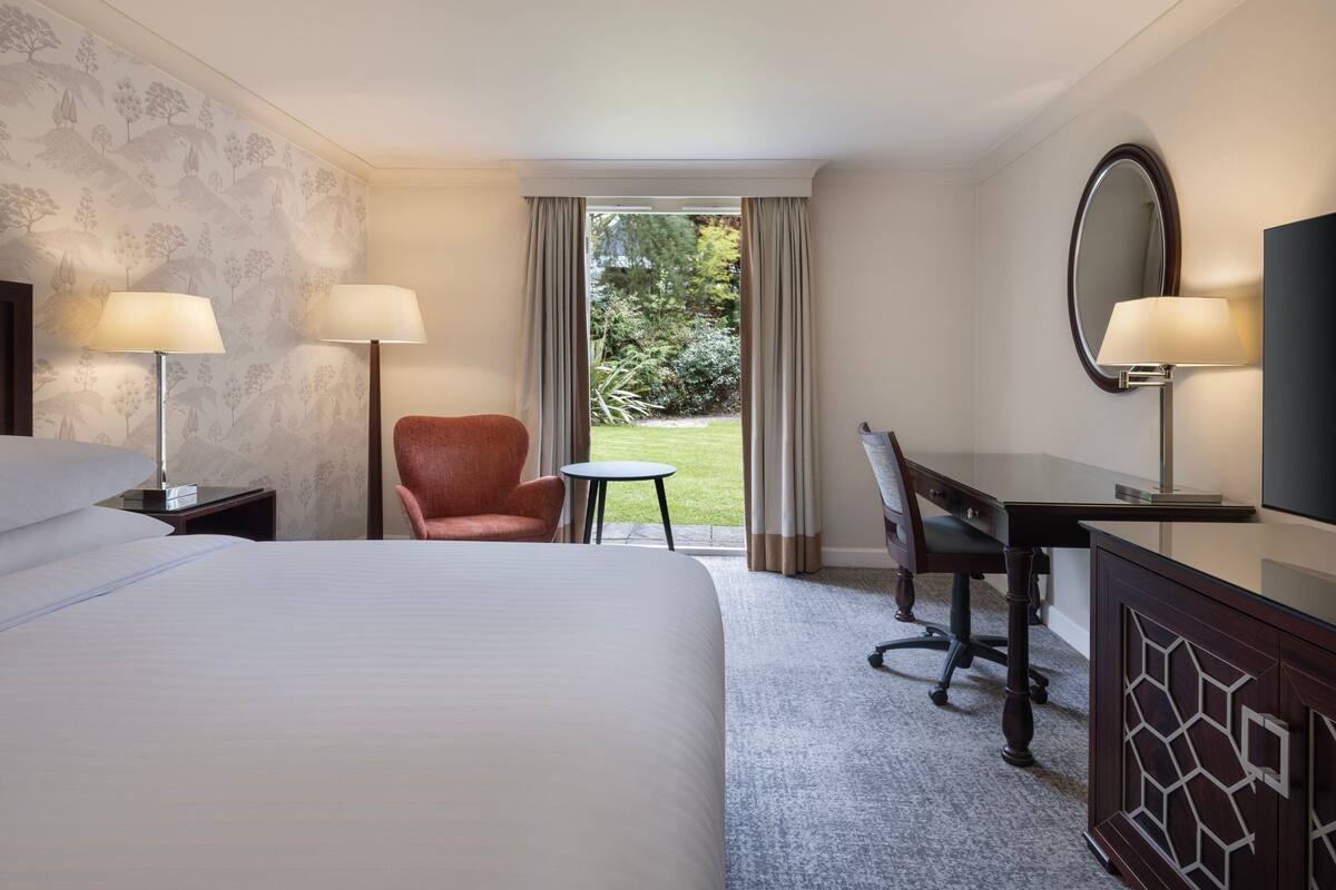 Habitación de hotel con una cama grande, dos lámparas de noche, un escritorio con silla, televisor y vistas al exterior.