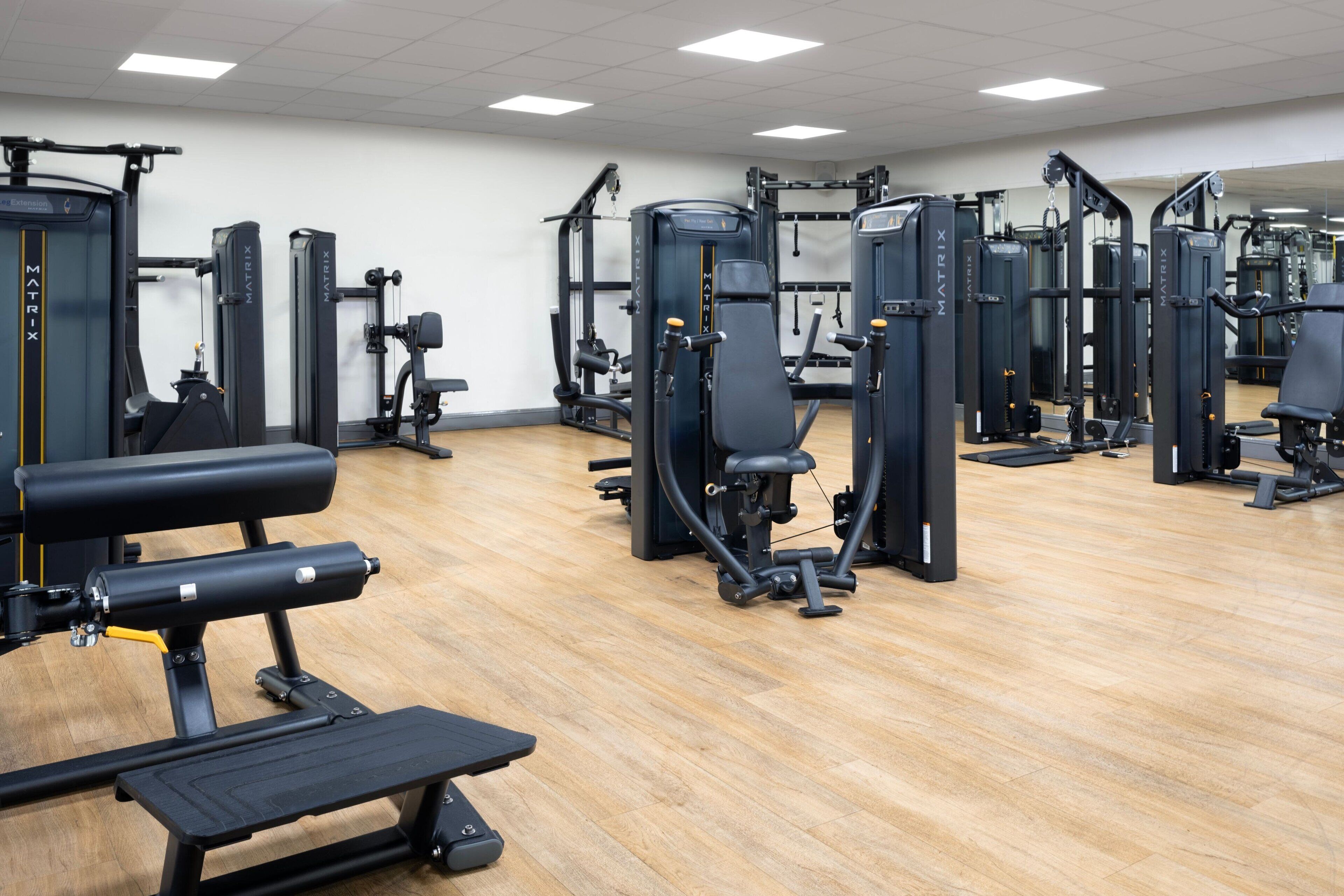 Une salle de sport équipée de divers appareils d’exercice, de bancs et dotée d’un plancher en bois.