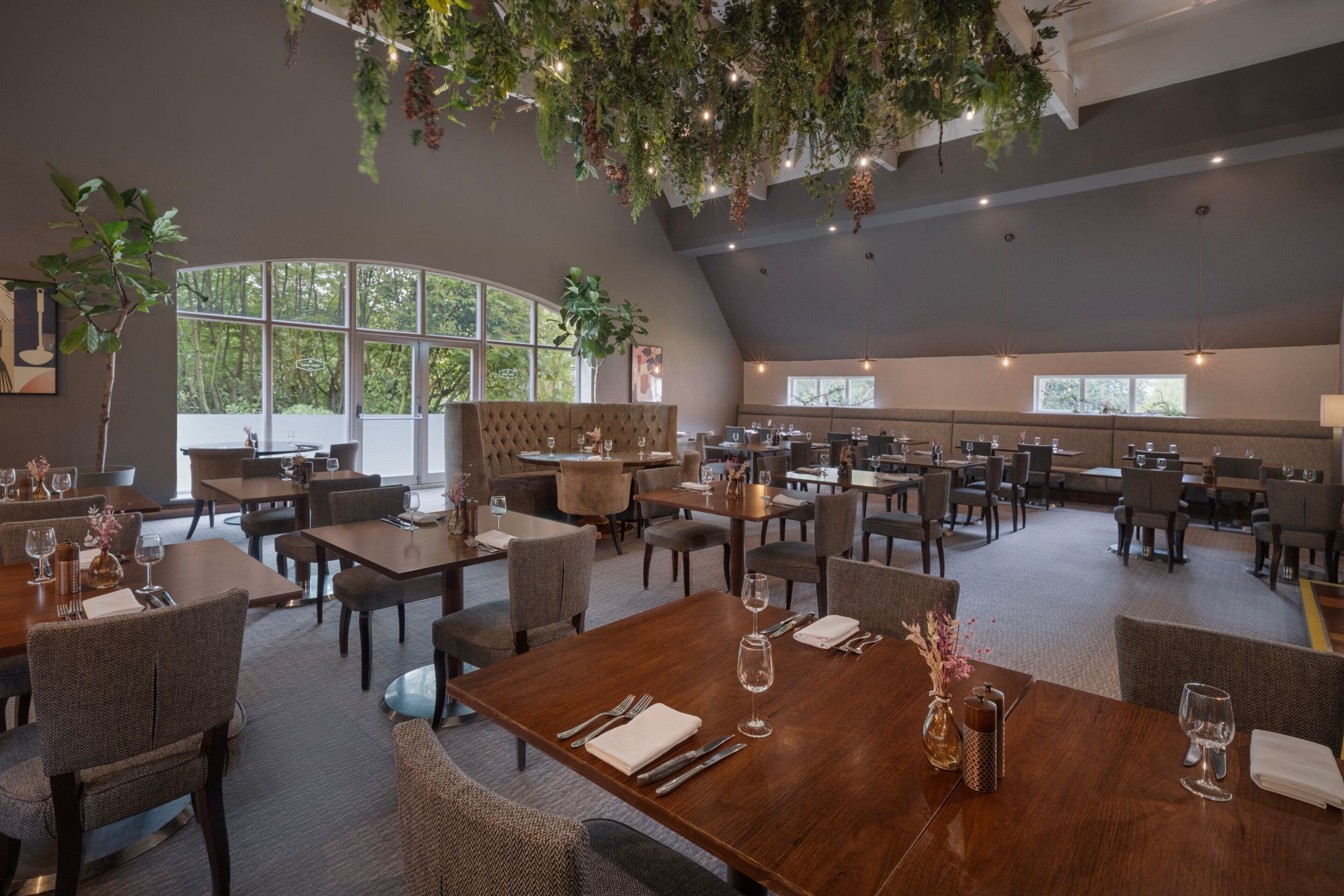 En rymlig restaurang med högt i tak, stora fönster och en mängd olika sittarrangemang, inklusive bord och avskilda sittplatser.