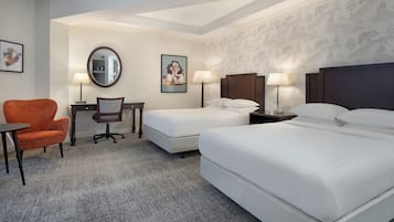 A hotel room with two beds, a desk, a chair, and two lamps.
