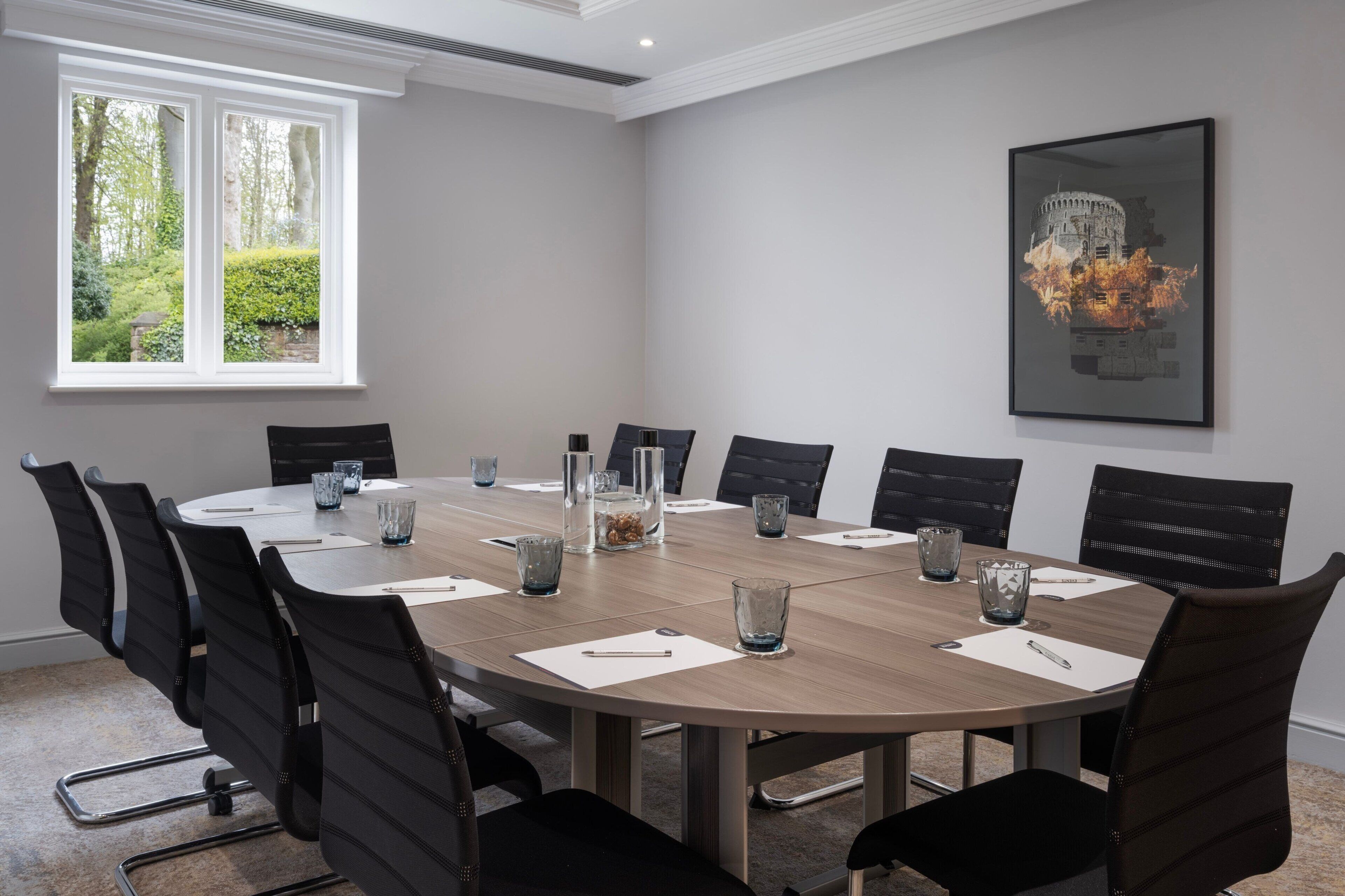 A conference room with a round table, black chairs, and a framed picture on the wall.