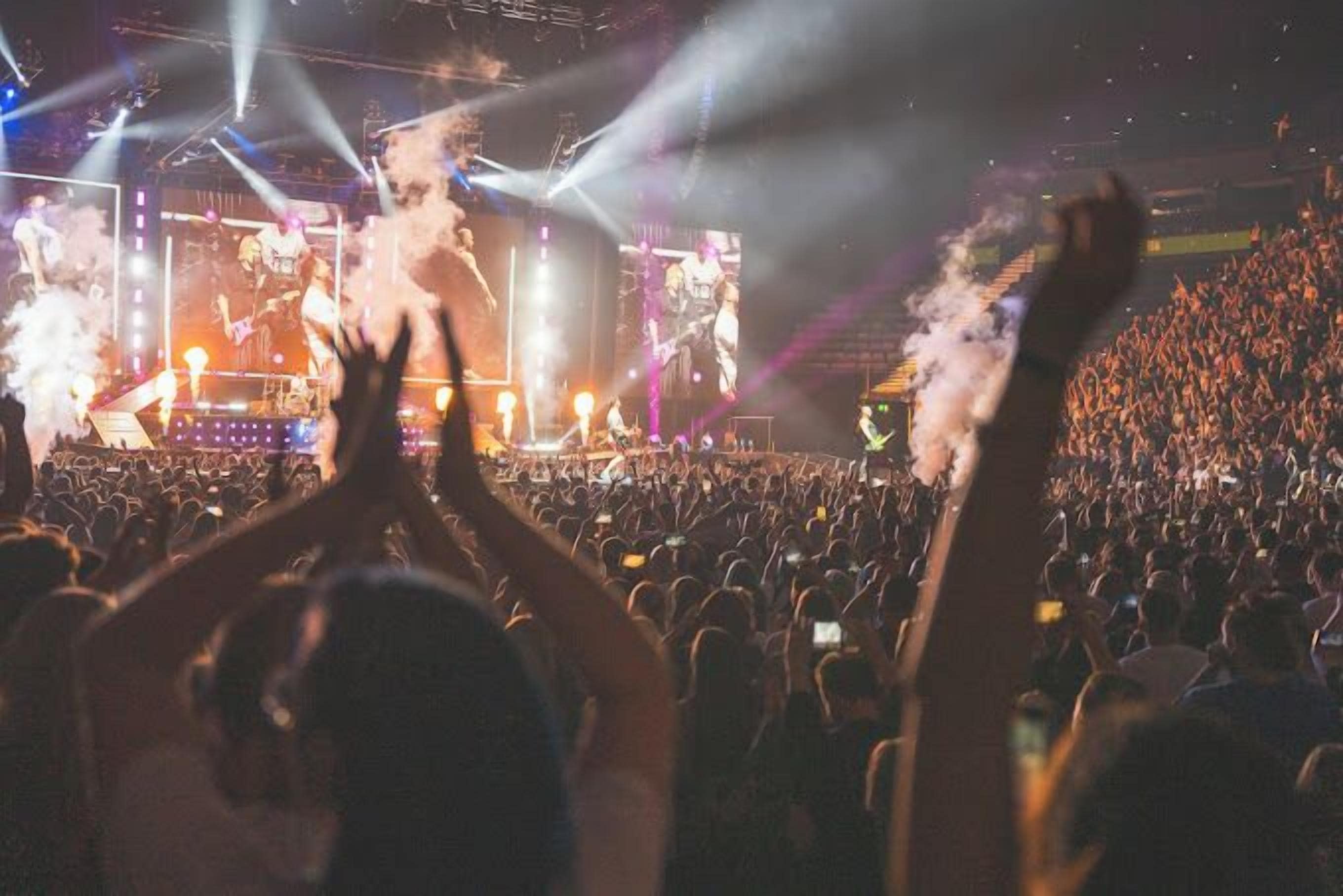 Een concert met een groot publiek, podiumverlichting en rookeffecten.