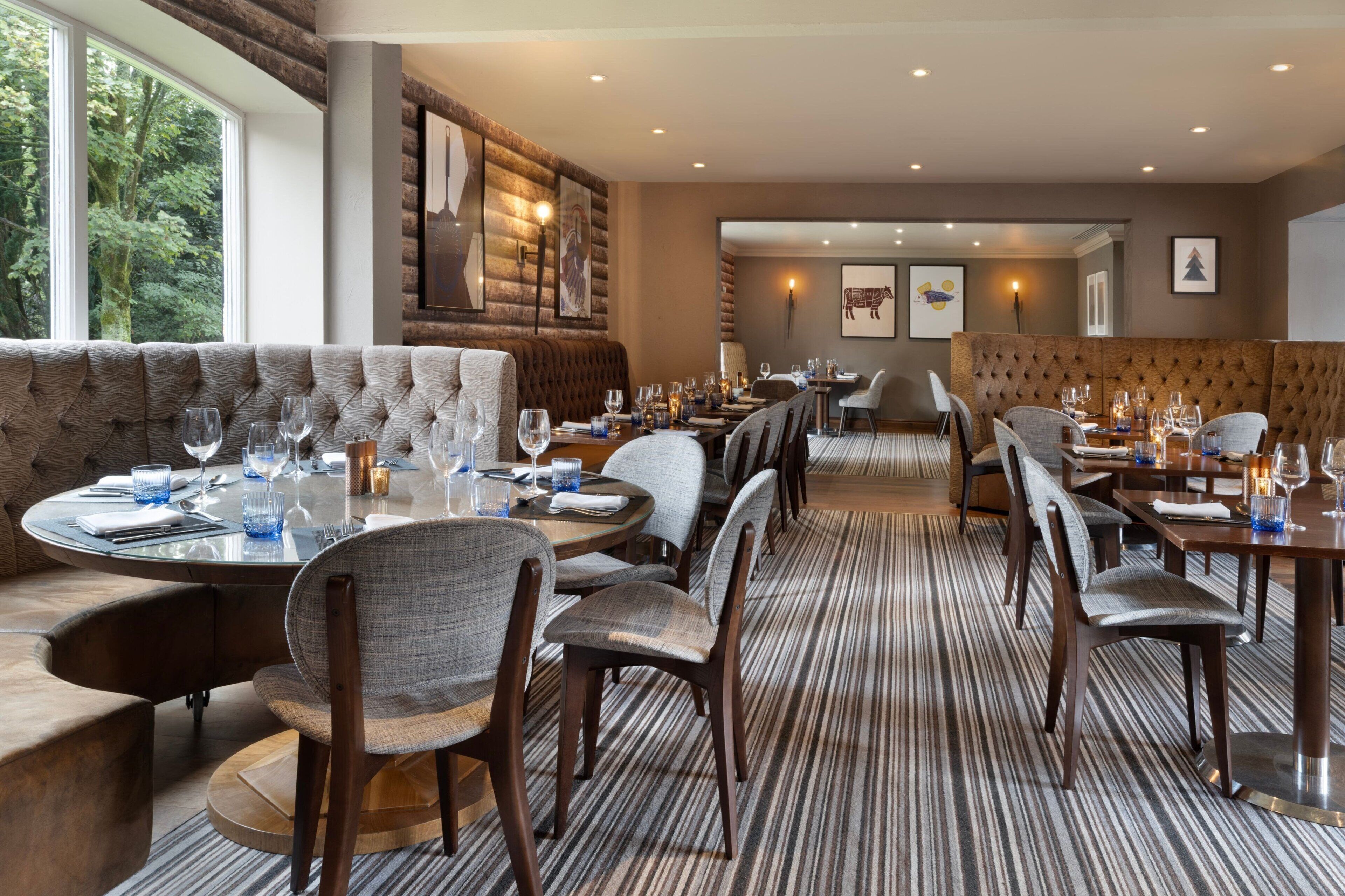 A restaurant with a mix of round and rectangular tables, upholstered seating, and a striped carpet.