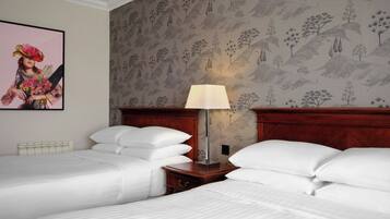 Habitación de hotel con dos camas, una mesita de noche con lámpara y papel tapiz floral.