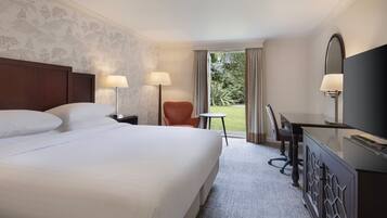 A hotel room with a large bed, two bedside lamps, a desk with a TV, and a view of the outdoors.