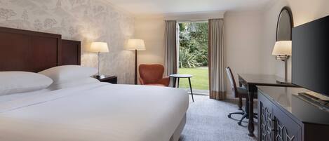 A hotel room with a large bed, two bedside lamps, a desk with a TV, and a view of the outdoors.