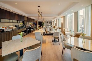 Comedor moderno de hotel con cocina al fondo, ventanas amplias y una variedad de opciones de asientos.