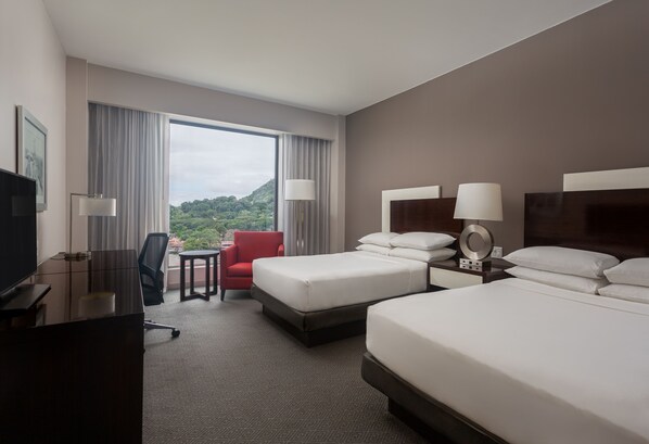 Habitación de hotel con dos camas, un escritorio, una silla y un televisor.